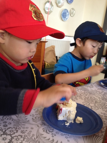 Birthday boy and his brother enjoying cake and their new firefighter caps.
